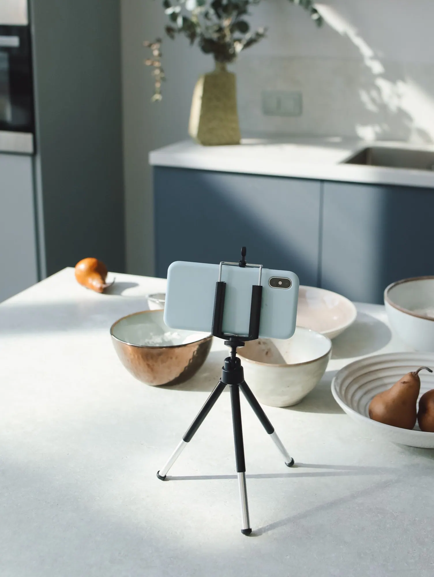 A phone on a small tripod on a kitchen counter, ready to record.